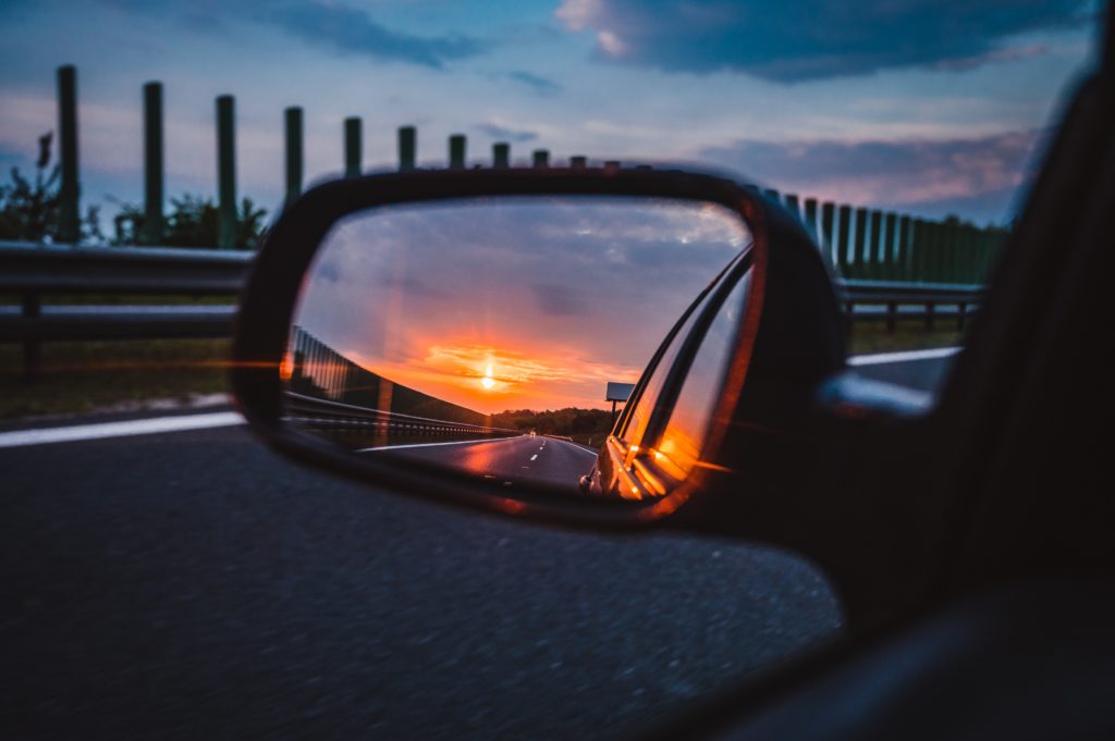 An image of the road behind through a car's sideview mirror at sunset